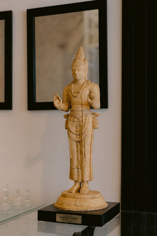 A replica Bodhisattva statue on a black plinth, set against framed mirrors