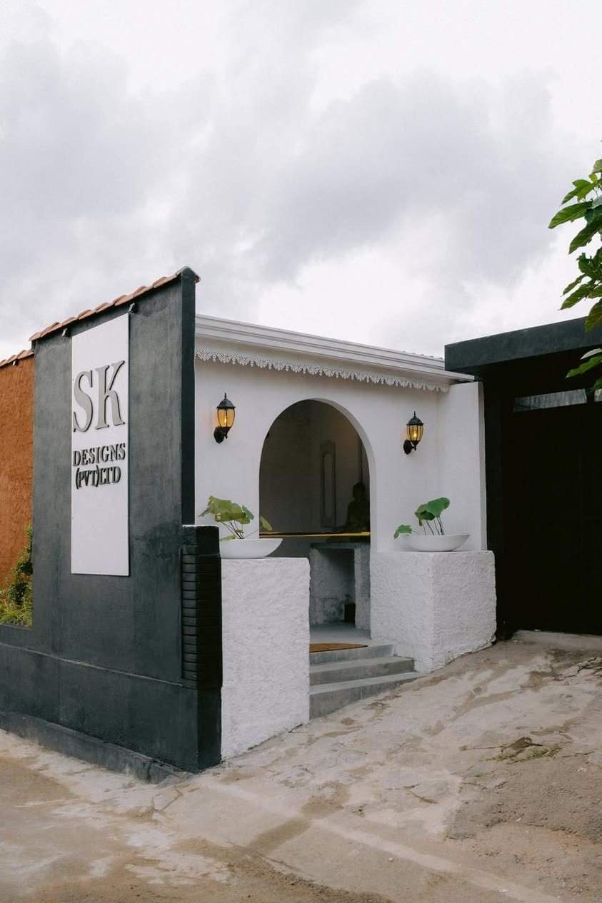 The studio frontage in Homagama: an arched entrance in white render set into a charcoal wall under a terracotta tiled edge, with the SK Designs sign on the left return