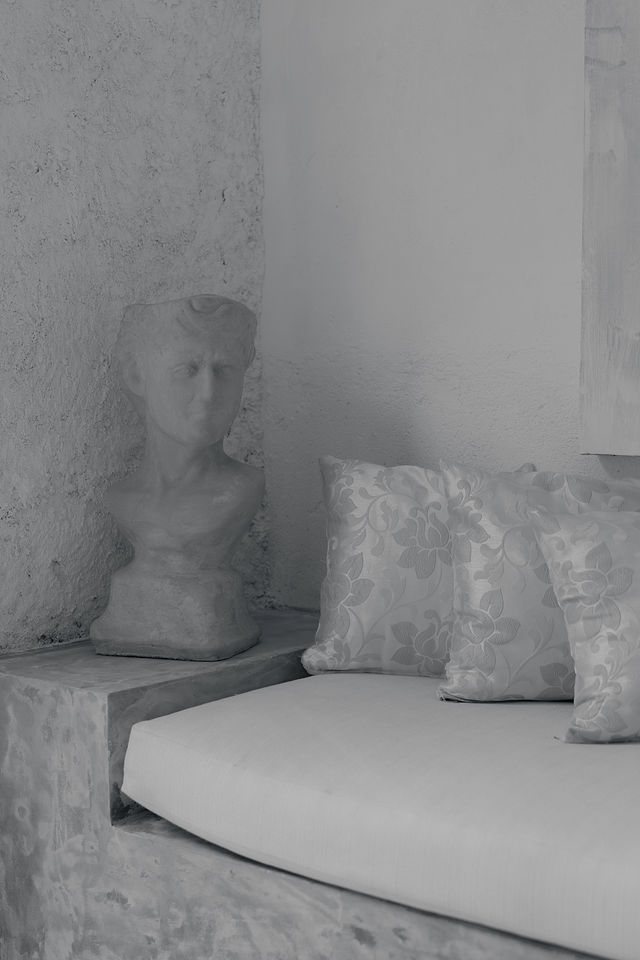 Built-in microcement seating with cushions, beside a classical bust set on a stepped plinth against a textured render wall